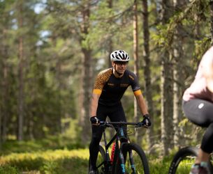 Cyklist i svart tröja och vit hjälm cyklar genom tät skog.