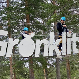 Barn och vuxen med blå hjälmar balanserar på bokstäverna i skylten