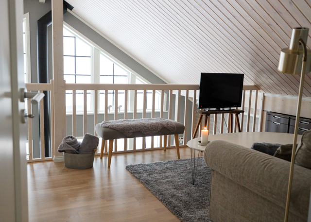 Bright loft with sofa, TV, bench, and sloped ceiling.