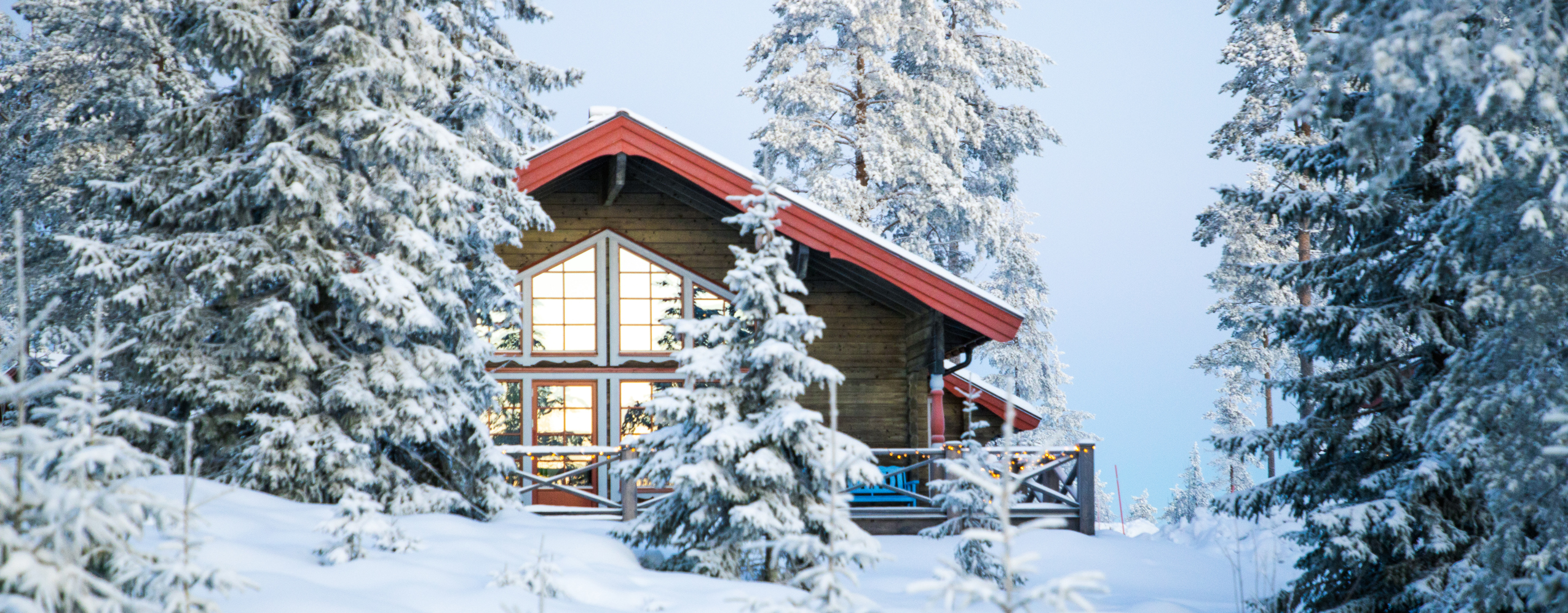 Træhytte med store vinduer og rødt tag i Orsa Grönklitt, omgivet af sneklædte grantræer.