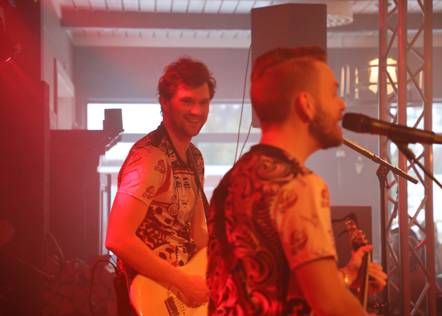 Närbild på två glada gitarrister som spelar och sjunger under en spelning.