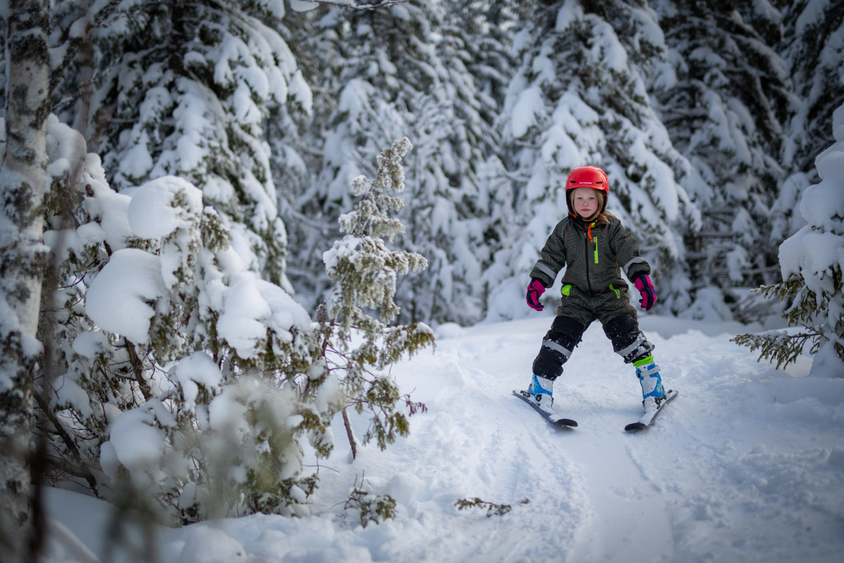 Child wearing a red helmet skiing on a snow-covered trail in the forest.