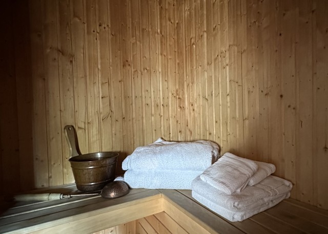 Wooden sauna with towels and a bucket with ladle placed on the bench.