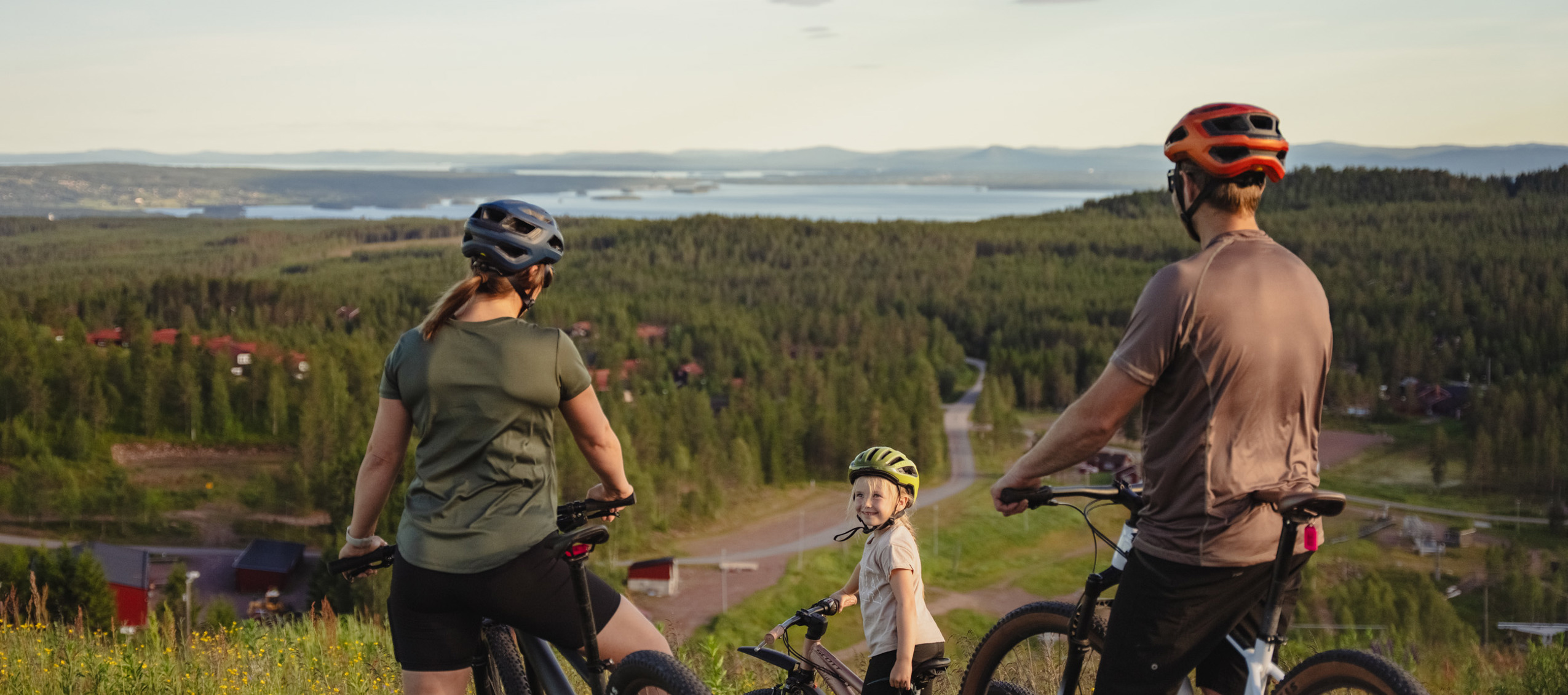 Familj med mountainbikes stannar för att njuta av utsikten över skog och sjö från en höjd i Orsa Grönklitt.