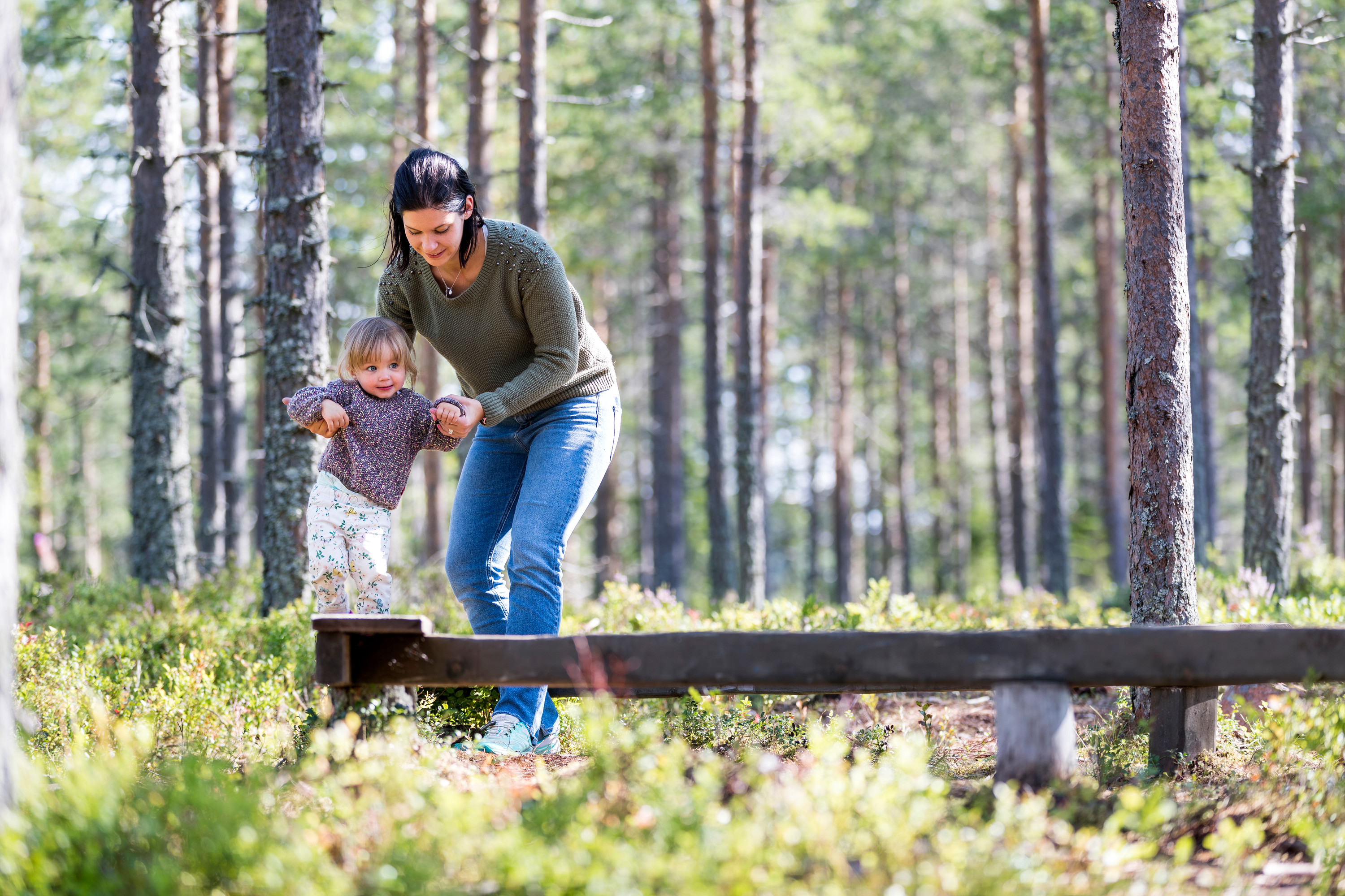 Adult and young child balancing together on a wooden beam in the forest.