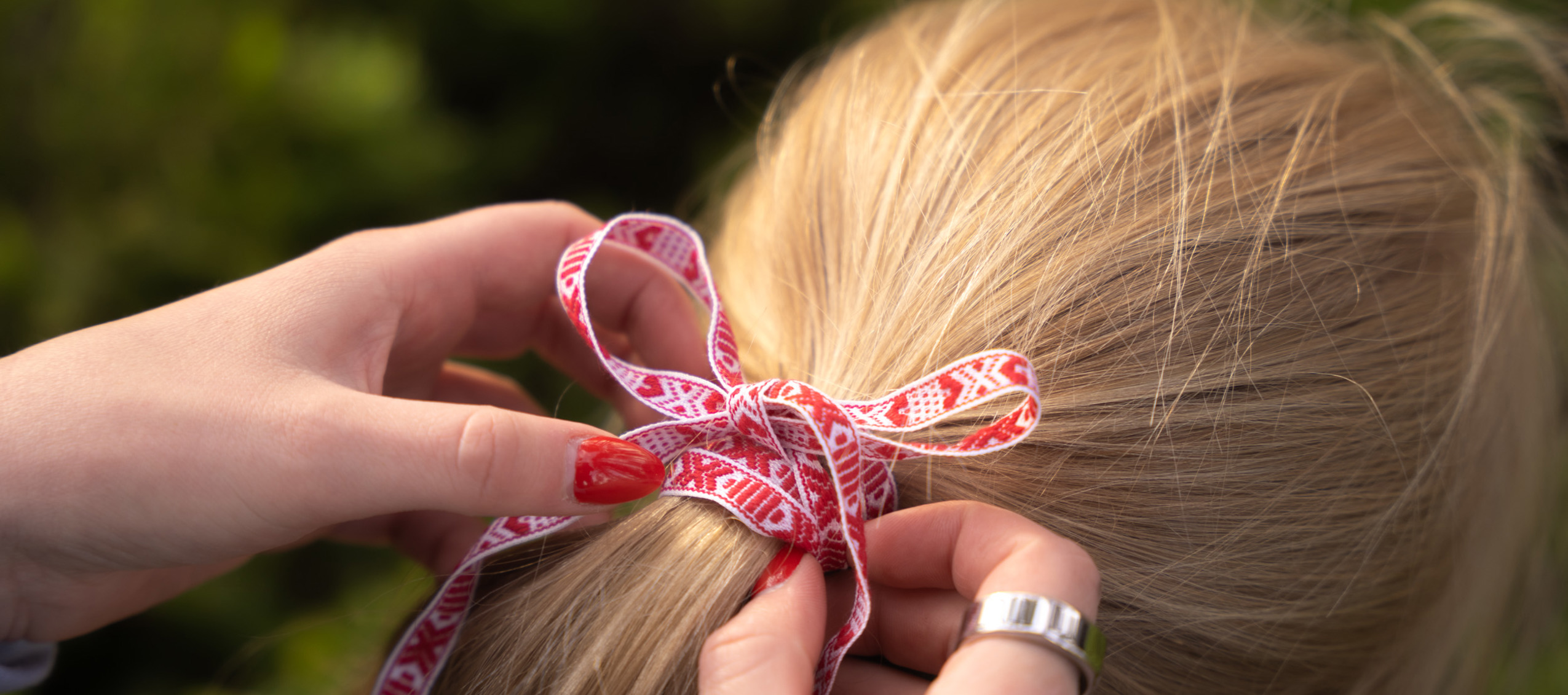 Händer knyter ett rött och vitt band i en fläta på ett barns hår.