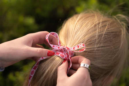 Hands tying a red and white ribbon into a braid in a child’s hair.