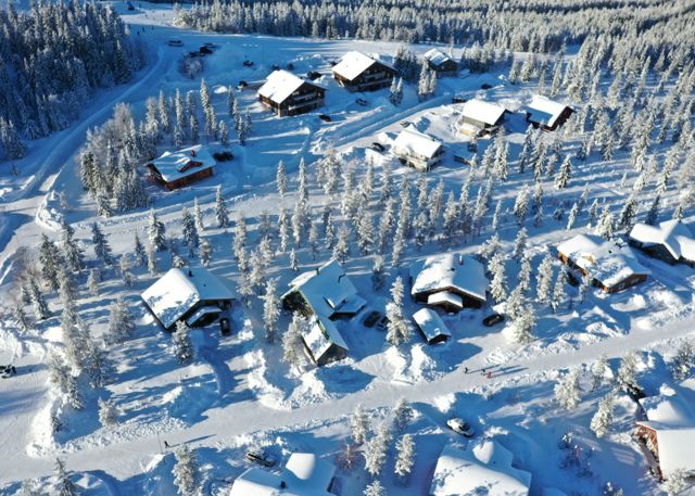 Flygfoto över fjällstugor i snötäckt skogsområde med vägar och vinterlandskap.