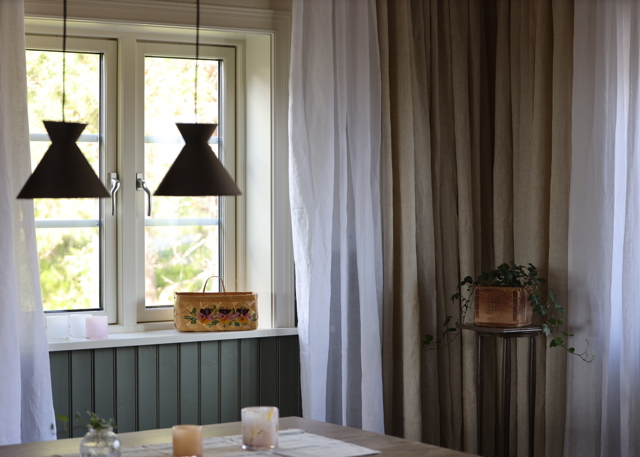 Window corner with curtains, two black pendant lamps, and table with candle holders.