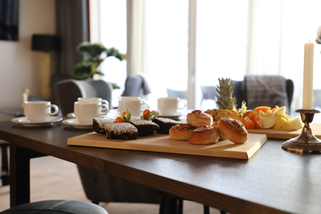 Dukat bord med kaffekoppar, frukt och fikabröd i ett ljust rum.