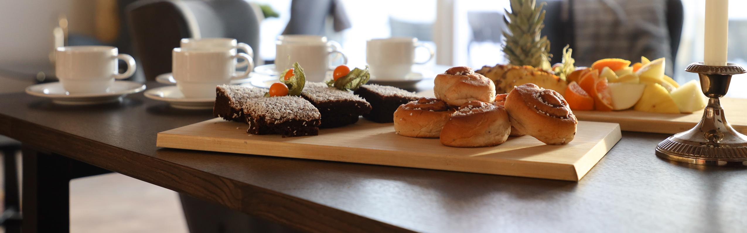 Set table with coffee cups, fruit, and pastries in a bright room.