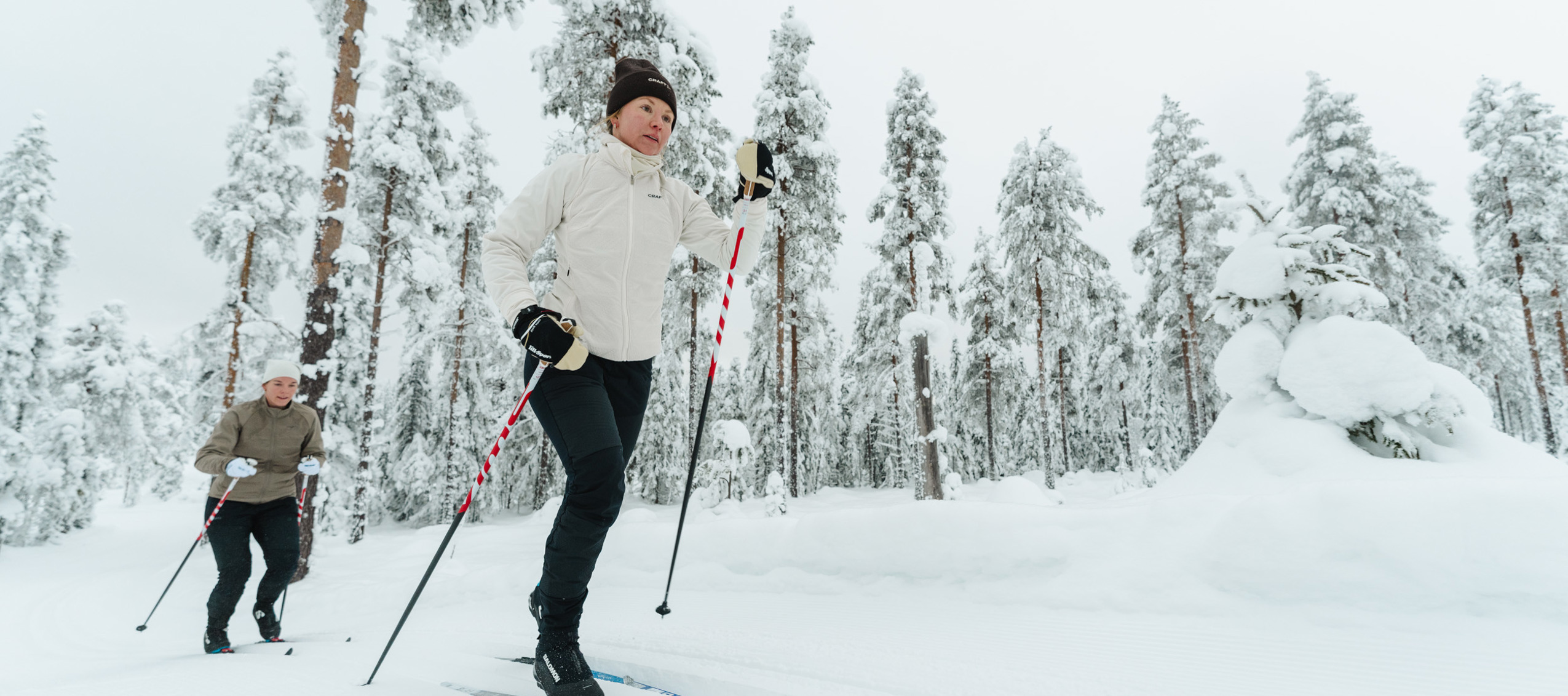 Två personer åker längdskidor på välpreparerade spår i ett snötäckt vinterlandskap.