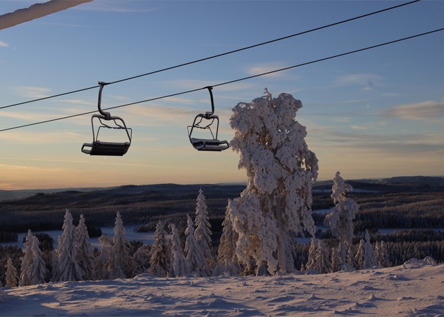 Tommma stolliftar svävar över ett snölandskap i solnedgången, med snötäckta träd och vidsträckt utsikt över bergen.