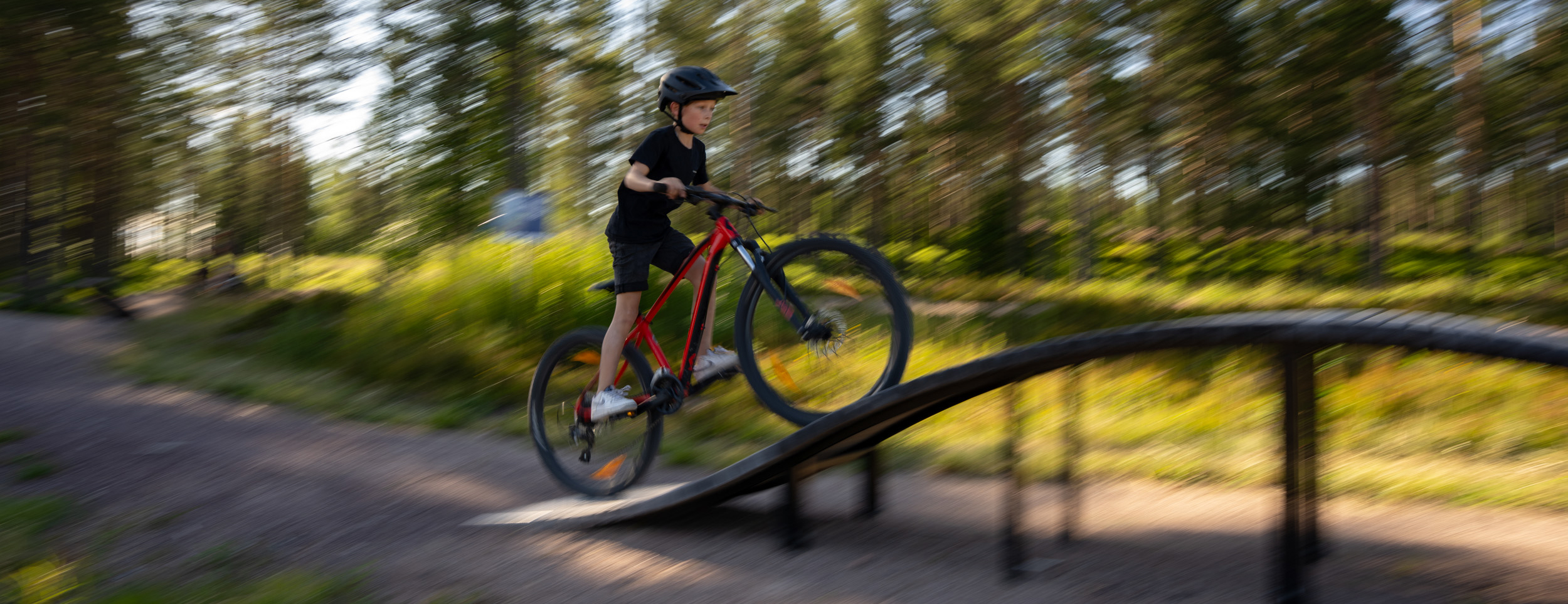 Barn cyklar över hinder på skills trail i skog