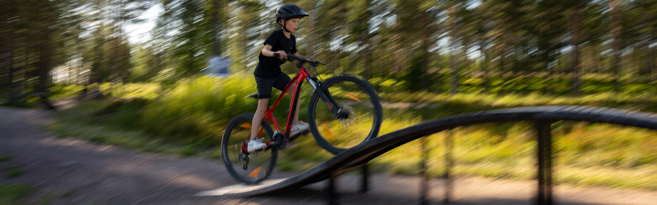Child riding over obstacle on skills trail in forest