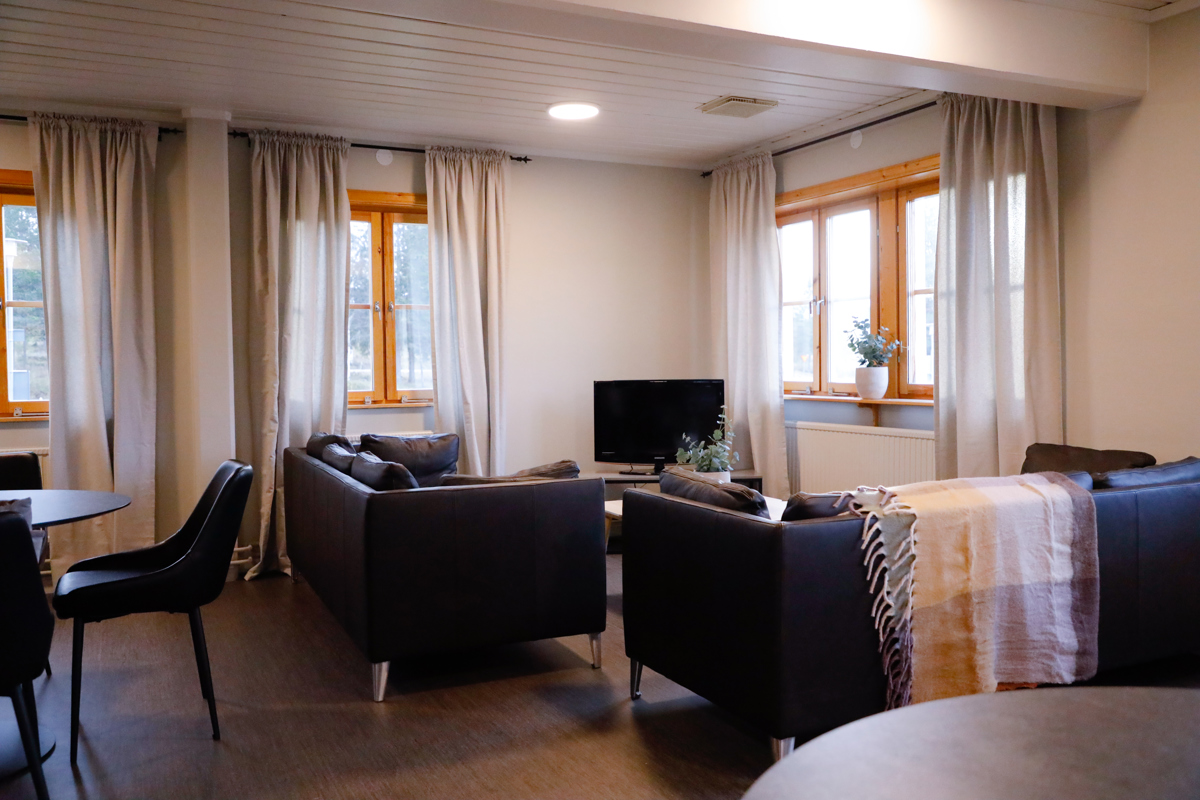 Sällskapsrum med två soffor, soffbord, TV och fönster med ljusa gardiner.