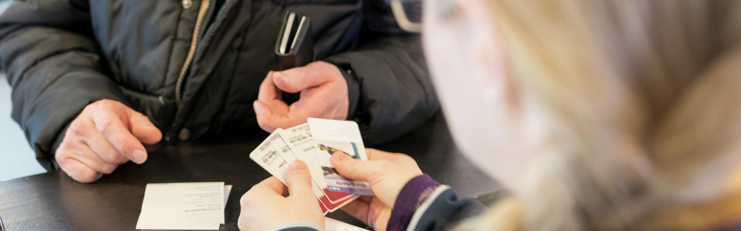 Person at a counter receiving tickets or a ski pass from staff wearing an Orsa Grönklitt-branded jacket.