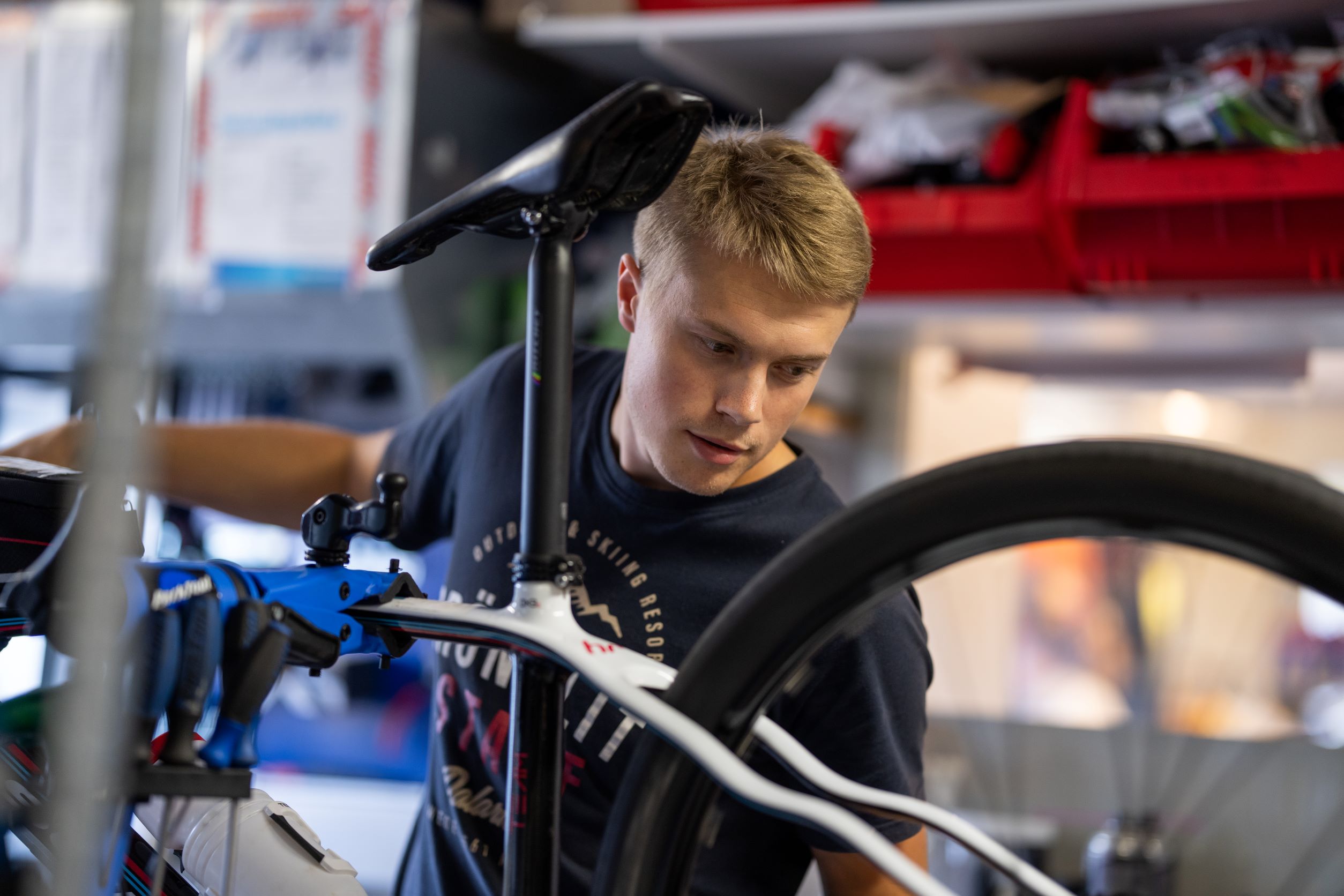 Young man in a black shirt adjusting a bicycle in a workshop.
