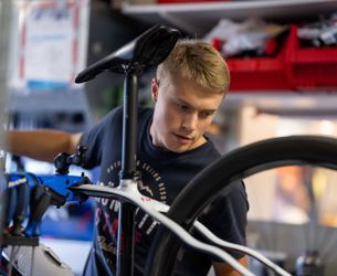 Ung man i svart tröja arbetar med att justera en cykel i en verkstad.