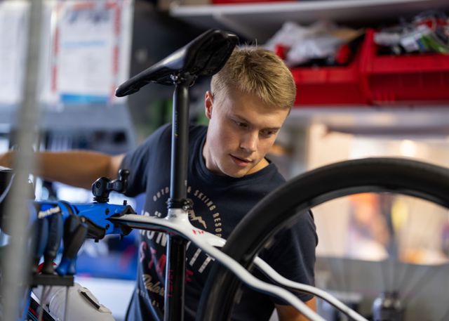 Ung man i svart tröja arbetar med att justera en cykel i en verkstad.