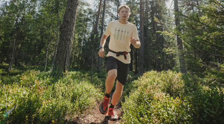 Person springer på smal stig genom grön skog