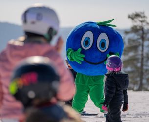 Maskoten Bärra möter barn i skidbacke, flera barn i hjälmar syns i förgrunden