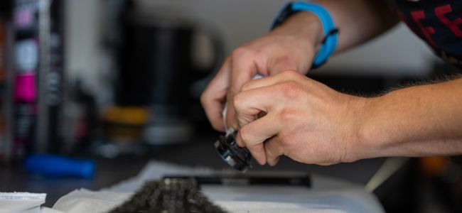 En person justerar en cykeldel i verkstaden, med fokus på händer och verktyg nära ett cykelnav.