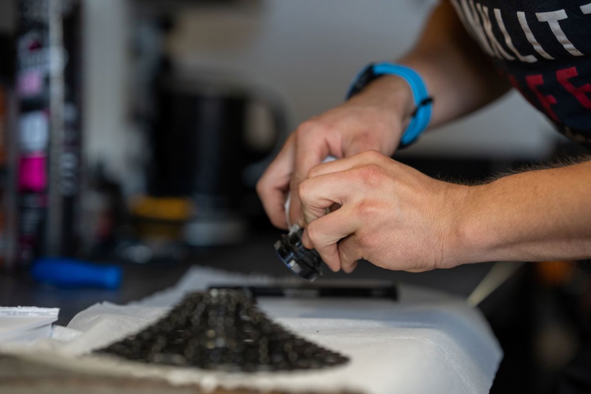 A person adjusts a bike component in the workshop, focusing on hands and tools near a bicycle hub.