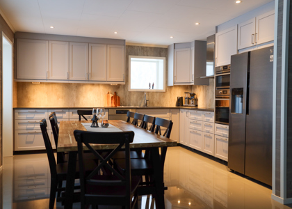 Stort modernt kök med grå skåp, rostfria vitvaror och matbord med stolar.