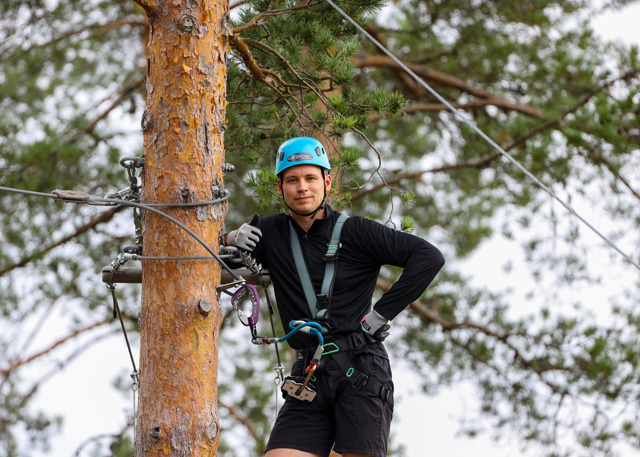 Man i klätterpark med sele vid träd ger tummen upp