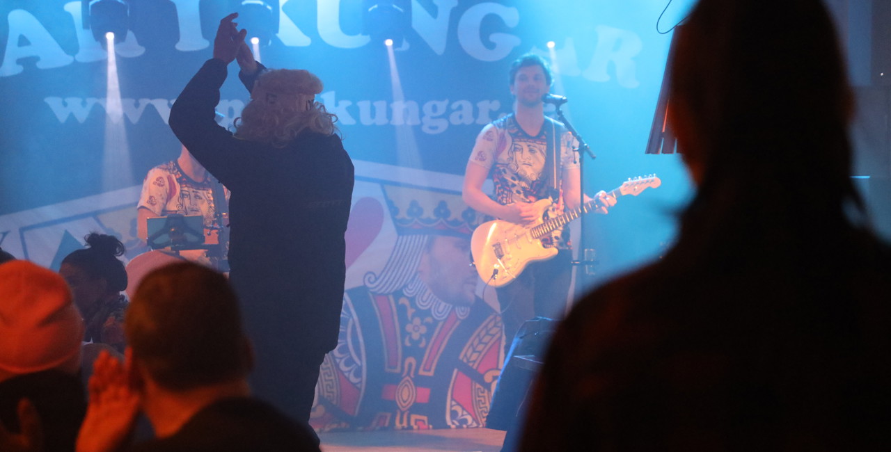 En sångare spelar gitarr på scen inför en publik under en kväll med livemusik.
