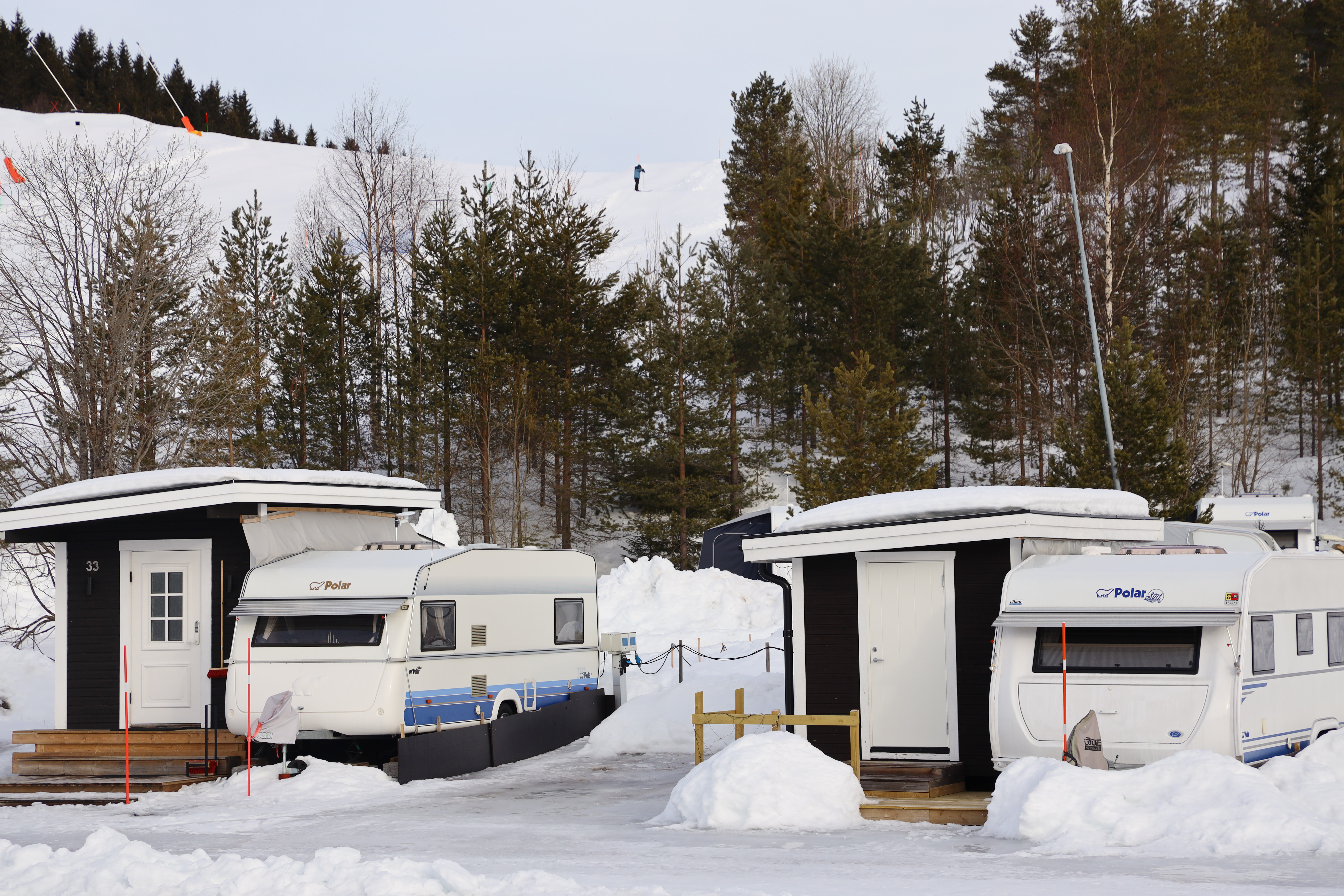 Campingvogne og servicebygninger placeret på en vintercampingplads omgivet af sne og skov.
