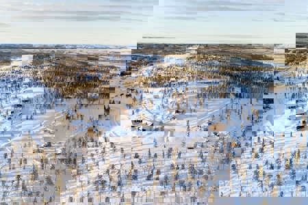 Flygvy över snötäckt skidområde med skog, byggnader och preparerade spår.