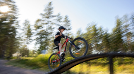 Barn cyklar över hinder på skills trail i skog