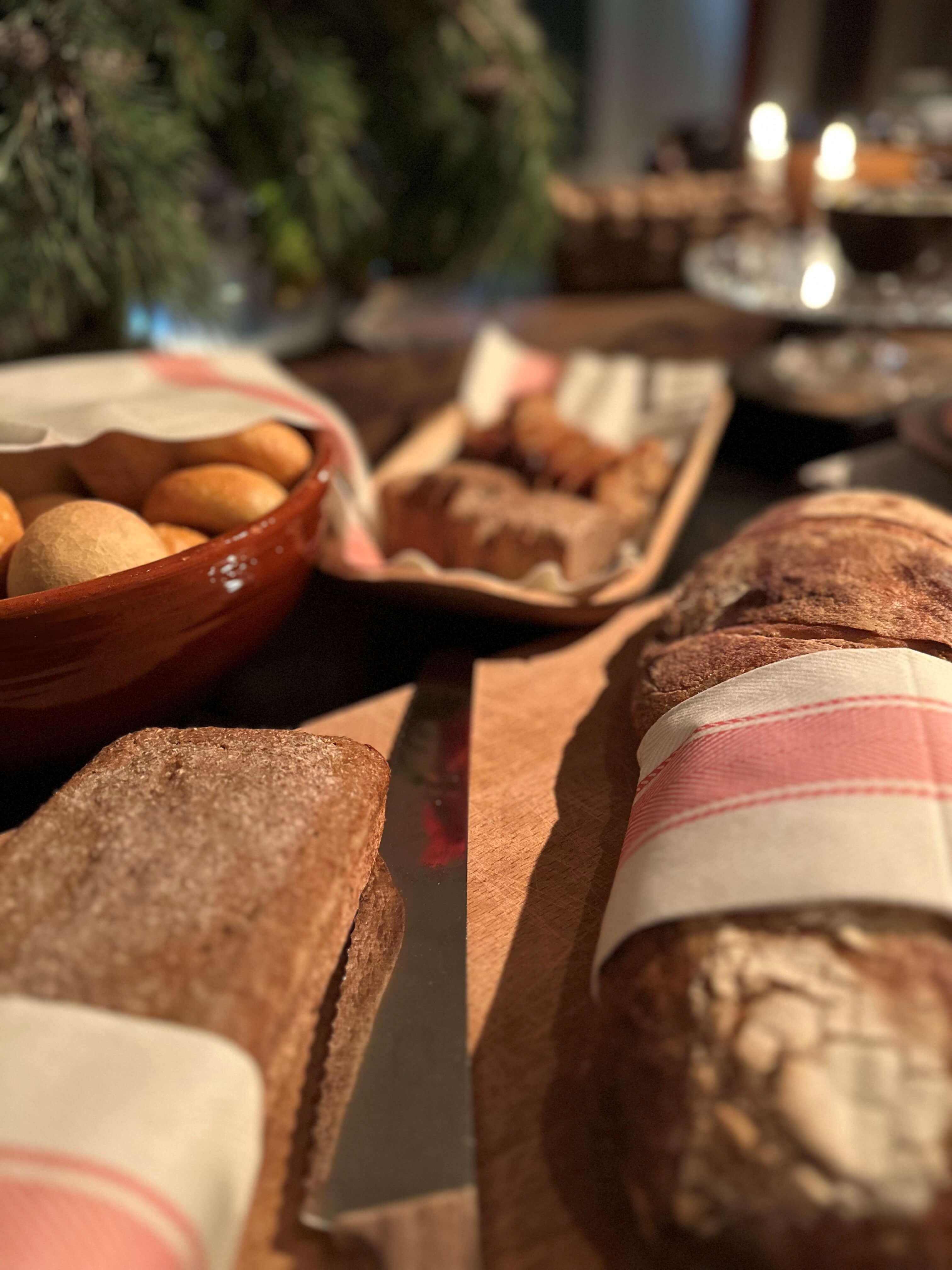 Close-up of freshly baked bread and small rolls on a wooden tray with a linen napkin.