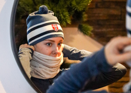 Ung kvinde med hue med Swix-logo, der ser sig i spejlet og justerer sin halsedisse inden en vinteraktivitet.