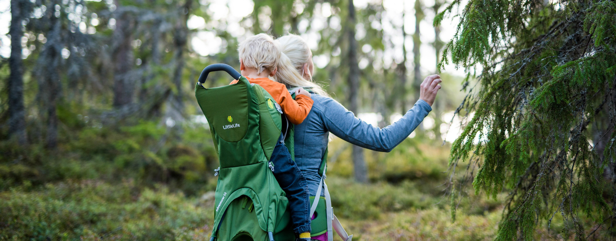 Adult carrying a child in a hiking carrier while exploring the forest at Orsa Grönklitt.