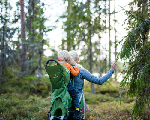 Adult carrying a child in a hiking carrier while exploring the forest at Orsa Grönklitt.