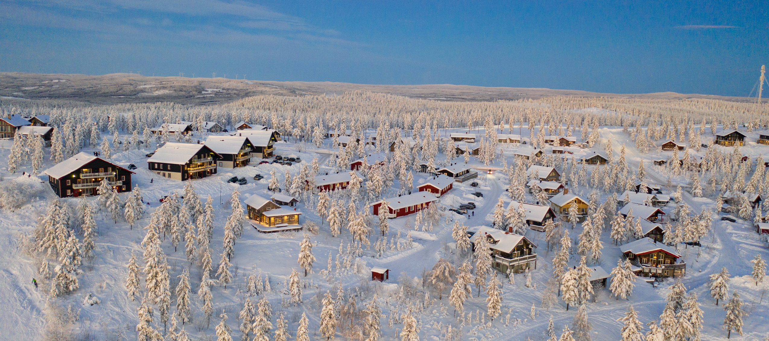 Flygfoto över Orsa Grönklitts stugområde i vinterskrud, med snötäckta träd och fjärran berg i bakgrunden.