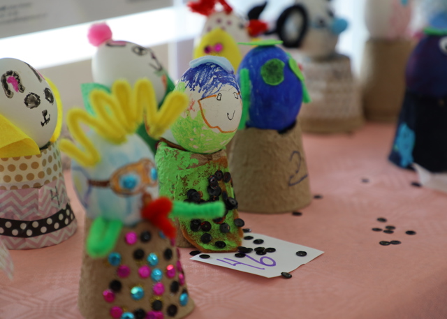 Färgglada dekorerade äggfigurer uppställda på bord, märkta med nummerlappar.