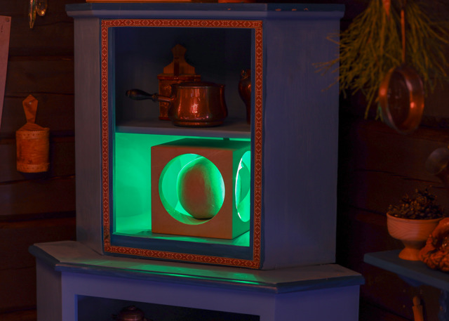 Shelf with a green-lit compartment containing a round object inside a square frame, surrounded by kitchen items in a wooden interior.