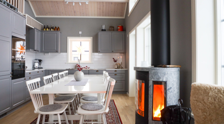 Kök med grå skåp, vitt matbord och braskamin i ett rum med högt i tak.