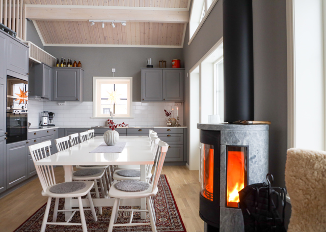 Kitchen with grey cabinets, white dining table, and wood-burning stove in a room with high ceiling.