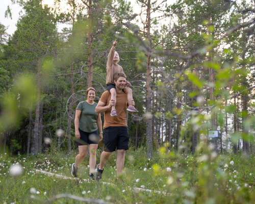 Barn på vuxens axlar pekar framåt under vandring i skog