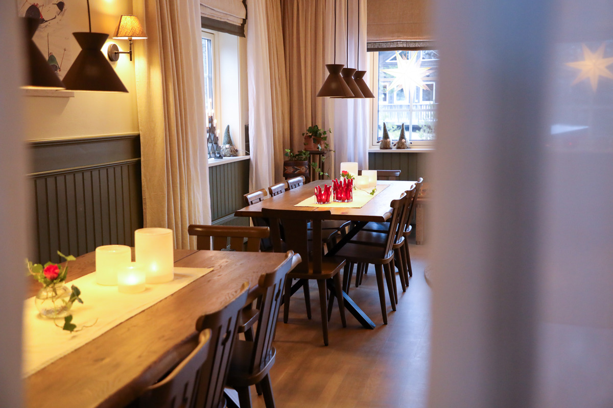 Dining room with two wooden tables, wooden chairs, candles, and window decorations.