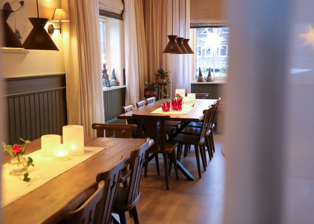 Dining room with two wooden tables, wooden chairs, candles, and window decorations.