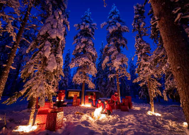 ”Snöklädd vinterkväll i skogen med människor klädda som jultomtar. De sitter vid en brasa och är omgivna av stora inslagna paket och upplysta granar.”